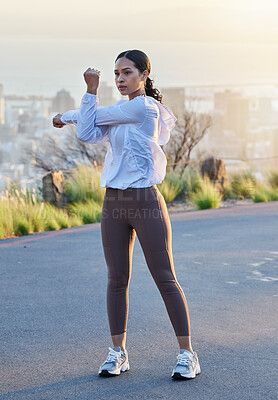 A female runner stretches her shoulders outdoors before a run.
